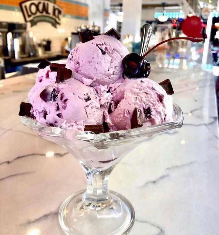 Scoops of berry ice cream with a cherry on top, in a glass coupe.