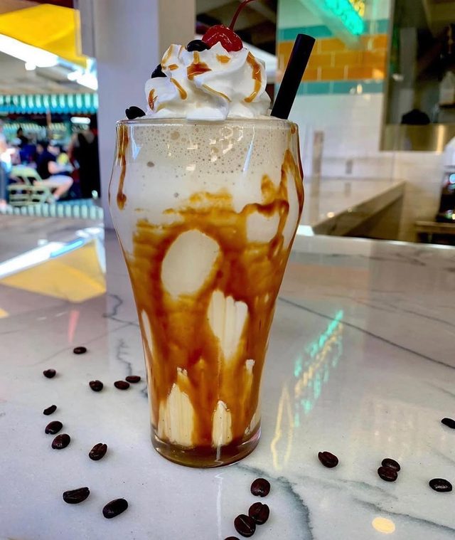 A tall caramel float with coffee beans scattered on the marble.
