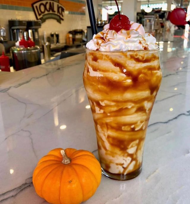 A tall caramel sundae glass on the counter, a small pumpkin beside it.