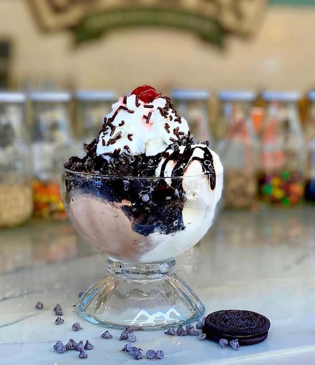 A footed glass of ice cream with chocolate sauce and biscuits, autumn decorations behind.